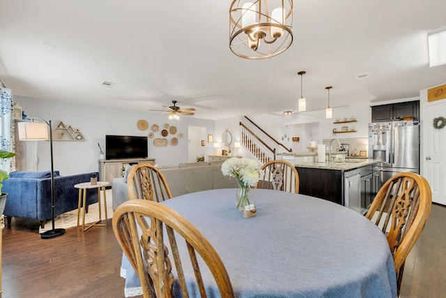 dining space featuring stairs, visible vents, dark wood-style floors, and ceiling fan with notable chandelier