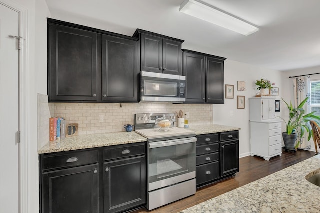 kitchen with decorative backsplash, dark wood-style flooring, light stone countertops, dark cabinetry, and stainless steel appliances
