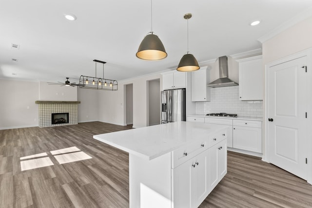 kitchen featuring a ceiling fan, stainless steel refrigerator with ice dispenser, crown molding, light countertops, and wall chimney exhaust hood