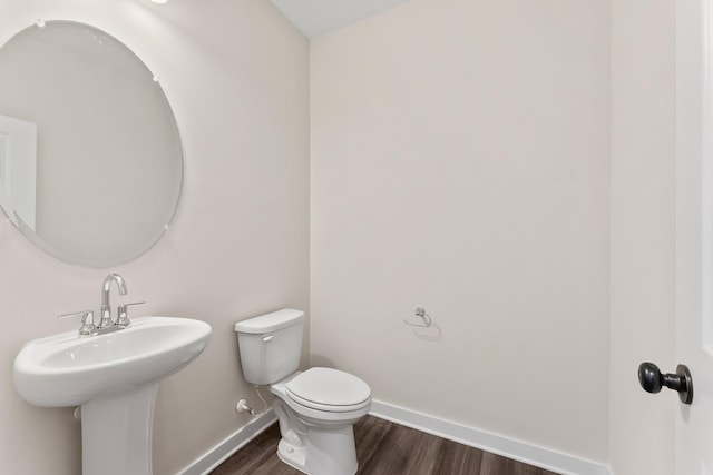 half bathroom featuring baseboards, a sink, wood finished floors, and toilet