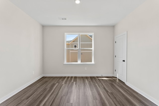 empty room with dark wood-style flooring, baseboards, and visible vents