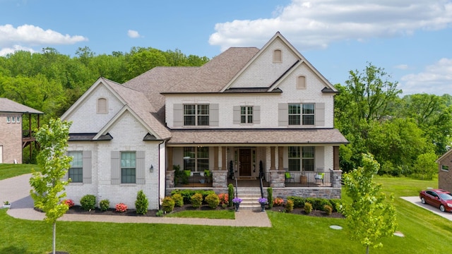 view of front of house featuring roof with shingles, a porch, brick siding, and a front yard