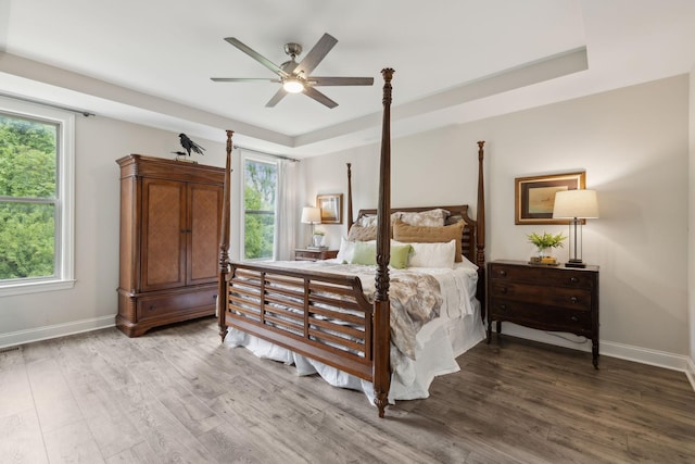 bedroom featuring ceiling fan, a raised ceiling, baseboards, and wood finished floors