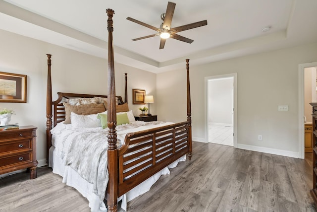 bedroom featuring baseboards, wood finished floors, and a tray ceiling