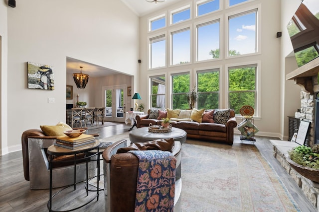 living room with a towering ceiling, wood finished floors, a chandelier, and a fireplace