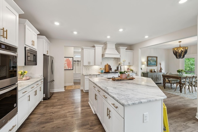 kitchen with decorative backsplash, a center island, premium range hood, stainless steel appliances, and white cabinetry