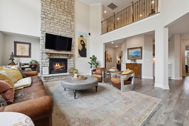living area featuring a stone fireplace, visible vents, wood finished floors, baseboards, and a high ceiling