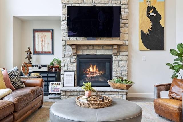 living room with baseboards, a stone fireplace, and wood finished floors