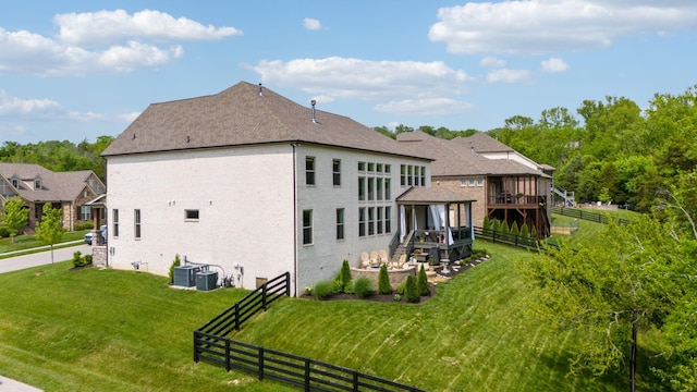 rear view of property with fence, a deck, brick siding, a shingled roof, and a lawn