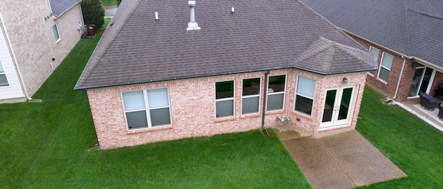 exterior space featuring a shingled roof, brick siding, french doors, and a yard
