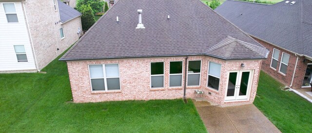 rear view of house featuring a shingled roof, brick siding, french doors, and a lawn
