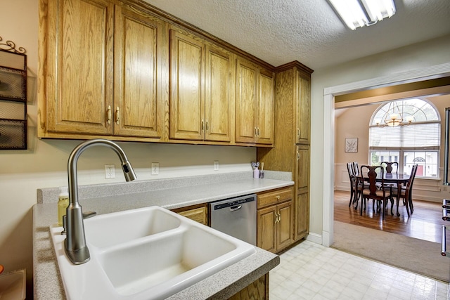 kitchen featuring brown cabinets, a notable chandelier, a sink, dishwasher, and light floors