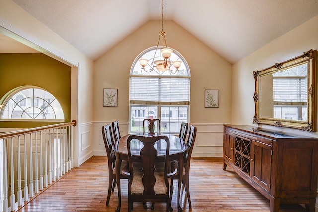 dining space with a decorative wall, lofted ceiling, light wood finished floors, and a wainscoted wall