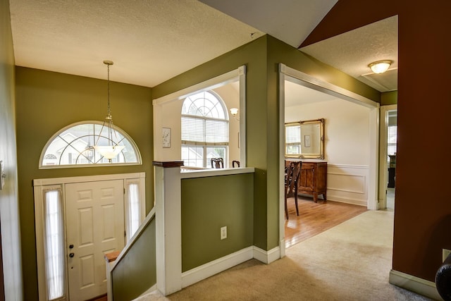 foyer entrance featuring baseboards, a textured ceiling, and light carpet