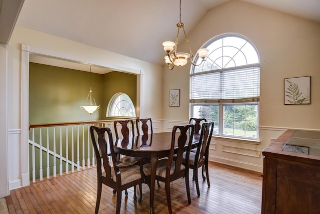 dining space featuring wood-type flooring, lofted ceiling, a wainscoted wall, and a chandelier