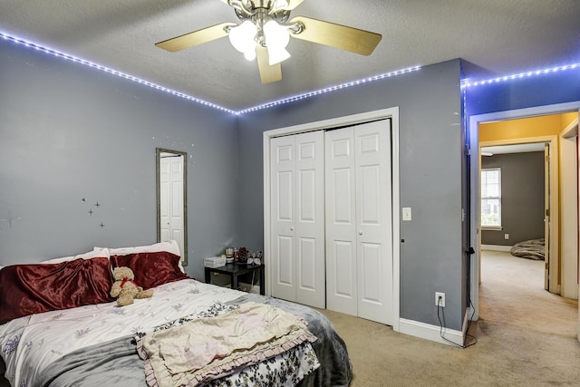 bedroom featuring ceiling fan, a textured ceiling, light colored carpet, baseboards, and a closet
