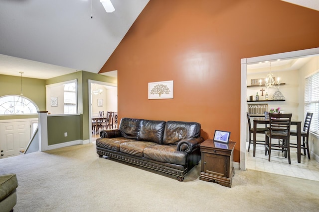 living area with high vaulted ceiling, baseboards, carpet, and ceiling fan with notable chandelier
