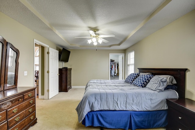 bedroom with ceiling fan, light carpet, a textured ceiling, baseboards, and a tray ceiling