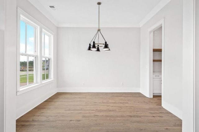 unfurnished dining area with visible vents, baseboards, a notable chandelier, light wood-style floors, and ornamental molding