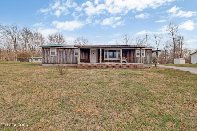 ranch-style home with a front lawn, covered porch, driveway, board and batten siding, and an outbuilding