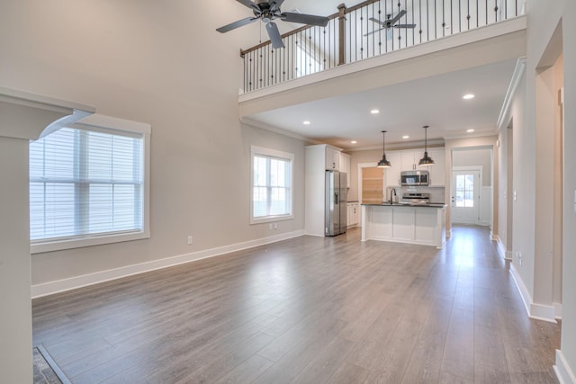 unfurnished living room featuring ceiling fan, crown molding, wood finished floors, a sink, and baseboards