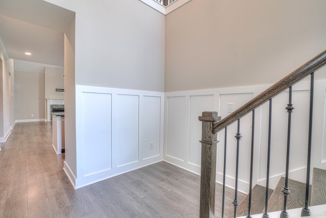 stairway featuring wood finished floors, recessed lighting, a decorative wall, and a wainscoted wall