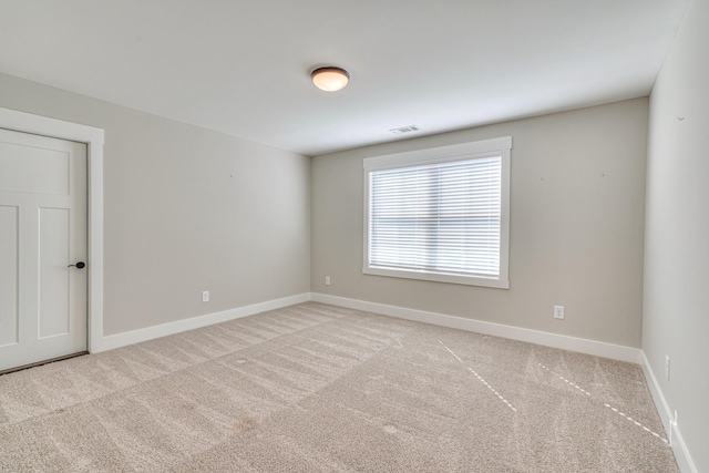 empty room with baseboards, visible vents, and light carpet