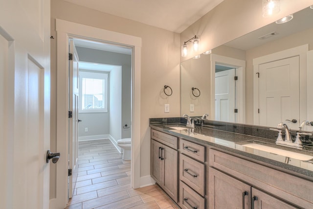 full bath with visible vents, double vanity, toilet, baseboards, and a sink