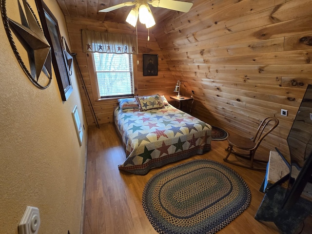 bedroom with a textured wall, ceiling fan, wood finished floors, and wooden walls