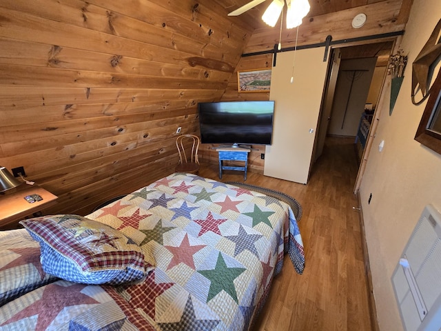 bedroom featuring a ceiling fan, visible vents, wood walls, a barn door, and wood finished floors