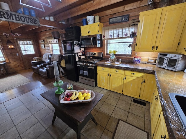 kitchen with a toaster, dark tile patterned floors, stainless steel appliances, and wood walls