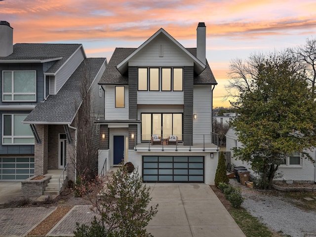 view of front facade featuring an attached garage, a shingled roof, driveway, and a chimney
