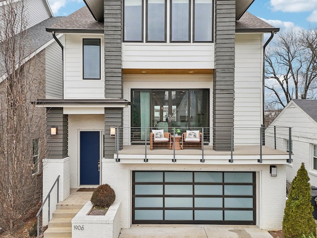 view of front of house featuring a garage, brick siding, a balcony, concrete driveway, and a shingled roof