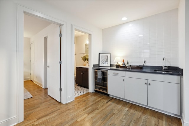 kitchen with beverage cooler, a sink, light wood-style flooring, and dark countertops
