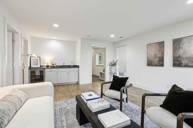 living area with light wood-style floors, beverage cooler, indoor wet bar, recessed lighting, and baseboards