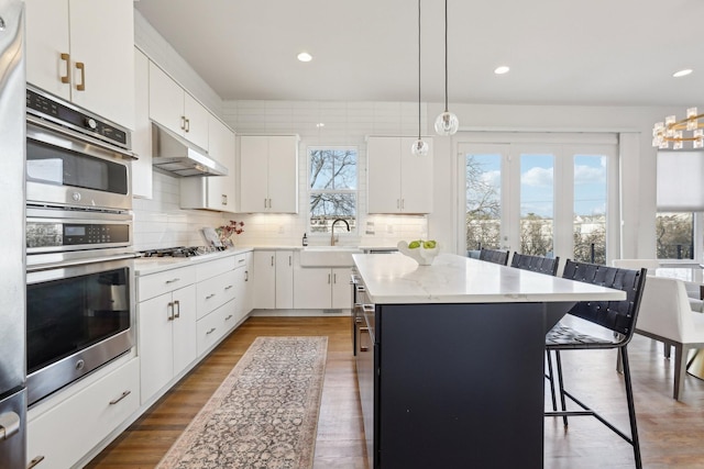 kitchen with backsplash, a kitchen bar, a center island, a sink, and under cabinet range hood