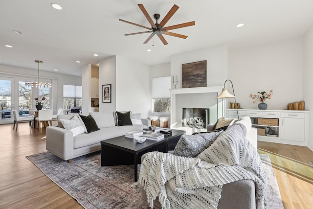 living room with a fireplace, ceiling fan with notable chandelier, recessed lighting, and wood finished floors