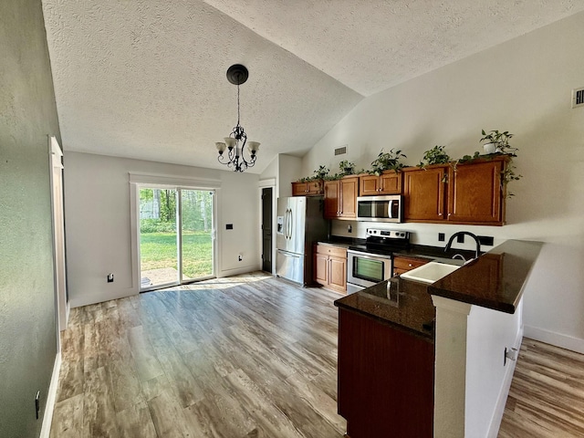 kitchen with dark countertops, a sink, brown cabinetry, light wood-style flooring, and stainless steel appliances
