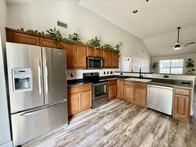 kitchen featuring a sink, visible vents, light wood-style flooring, stainless steel appliances, and vaulted ceiling