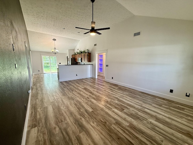 unfurnished living room with ceiling fan with notable chandelier, baseboards, vaulted ceiling, and wood finished floors