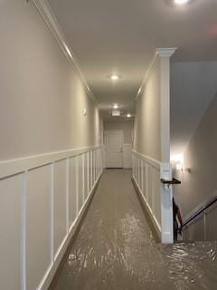 hallway featuring crown molding, a wainscoted wall, and a decorative wall