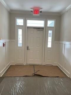 entryway with crown molding, a decorative wall, and a wainscoted wall