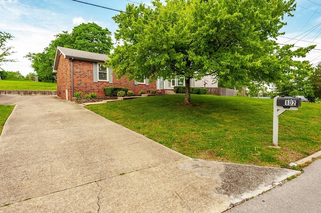view of front facade featuring fence, concrete driveway, a front lawn, and brick siding