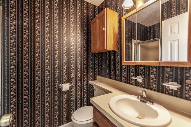 full bath featuring vanity, toilet, wallpapered walls, and a stall shower