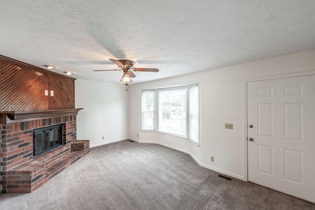 unfurnished living room with ceiling fan, a textured ceiling, a fireplace, baseboards, and carpet flooring