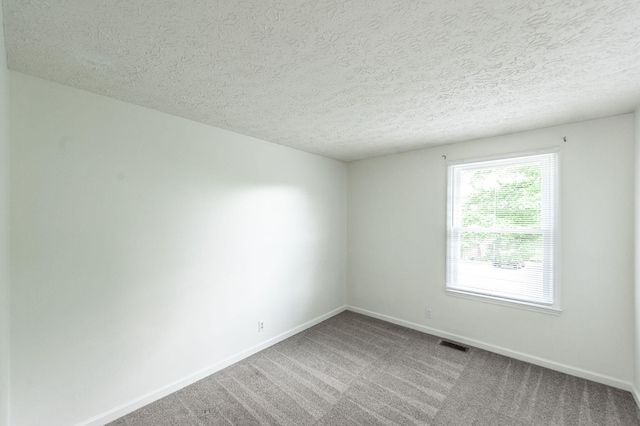 unfurnished room featuring carpet flooring, a textured ceiling, baseboards, and visible vents