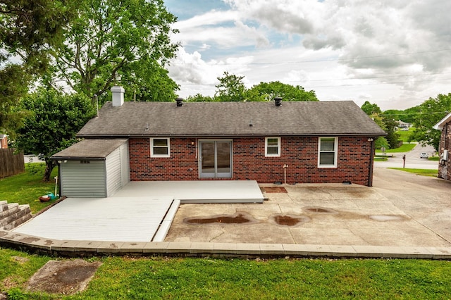 back of house with a chimney, roof with shingles, a deck, brick siding, and a patio