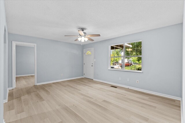 spare room featuring ceiling fan, light wood finished floors, a textured ceiling, baseboards, and visible vents