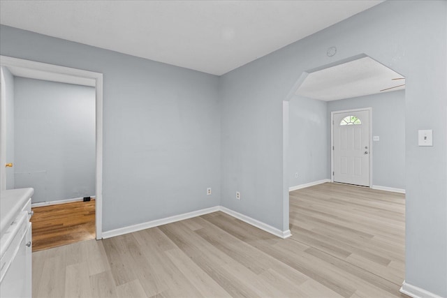 foyer with arched walkways, baseboards, and light wood finished floors