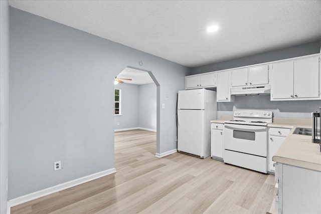 kitchen featuring arched walkways, light countertops, light wood finished floors, under cabinet range hood, and white appliances